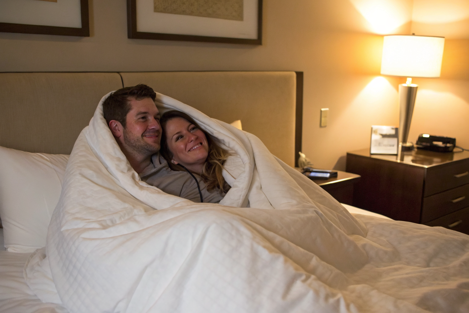 A couple (man and woman mid thirties) in a hotel room under duvet