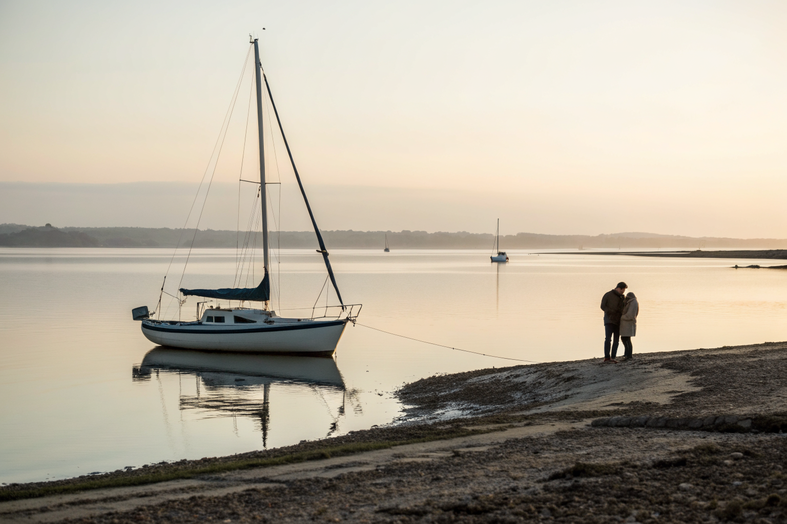 Een klein verankerd zeilbootje op kalm water bij een stille oever in het vroege ochtendlicht., passend bij onderliggende behoeften